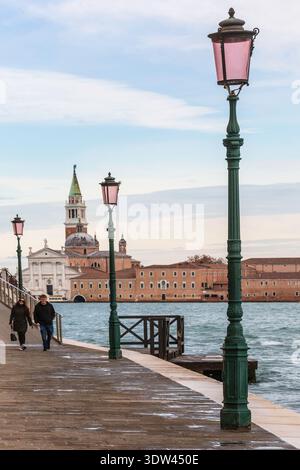 Ein Paar genießt einen ruhigen Spaziergang entlang der malerischen venezianischen Uferpromenade mit historischer Architektur im Hintergrund. Stockfoto