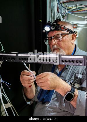 Techniker, der in einem Server-Rack arbeitet, um Netzwerkkabel anzuschließen und zu schließen. Das Bild repräsentiert die Dateninfrastruktur, Telekommunikation Stockfoto