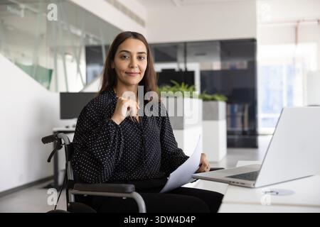 Positive junge Geschäftsfrau aus dem Nahen Osten mit Behinderung im Rollstuhl Stockfoto
