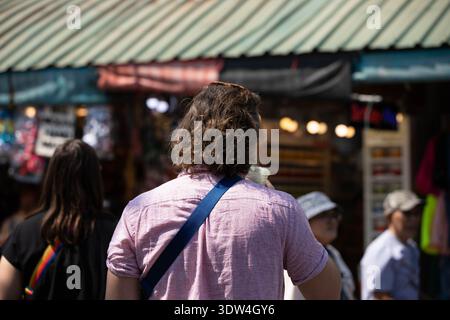 Mann trinkt Wasser aus Plastikbecher und erkundet den lokalen Markt, raues Tageslichtporträt, Rückansicht, auf dem Chatuchak Markt. Stockfoto