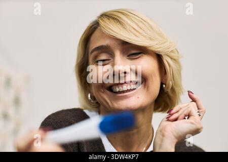 Kaukasische reife Frau lächelt und hält Schwangerschaftstest, zeigt Aufregung und Glück, fokussiert auf Femtech und Frauengesundheit, Nahaufnahme von fröhlichem Gesichtsausdruck Stockfoto