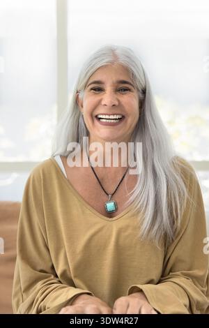 Lachende reife Frau posiert für die Kamera auf der Couch Stockfoto
