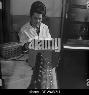 Das historische Schwarzweiß-Porträt der 1970er Jahre zeigt eine fokussierte Wissenschaftlerin in einem weißen Mantel, die in einem Labor der Fischfarm „Donrybkombinat“ im Bezirk Slawjansk, Region Donezk, ukrainische SSR, UdSSR arbeitet. Sie bedient sorgfältig ein optisches Vintage-Messgerät mit Glaskolben, die auf dem Schreibtisch stehen. Dieses authentische Archivfoto zeigt die wissenschaftliche Kontrolle der Wasserqualität in der sowjetischen Aquakultur, professionelle Arbeit und die ruhige Atmosphäre im friedlichen Donbass vor dem Krieg, die die regionale Industrie widerspiegelt. Stockfoto