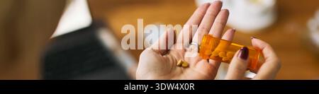 Weiße Frau hält verschreibungspflichtige Flasche und gießt gelbe Tabletten in die Palme, mit Medikamenten für Gesundheitsmanagement mit Laptop im Hintergrund, veranschaulicht Femtech Kontext Stockfoto
