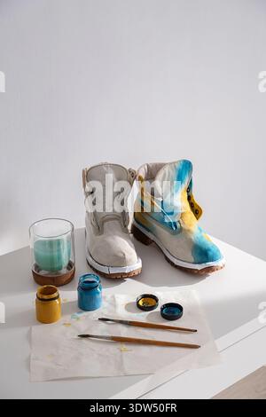 Unfertiger, individueller Schuh und ein Schuh, der mit Farben, Pinseln bemalt wird. Design-Konzept für handgefertigte Schuhe. Stockfoto