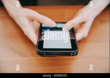Nahaufnahme von Händen, die ein Smartphone und eine Kreditkarte über einem Holztisch halten, was mobile Bezahlung, Online-Shopping und sichere digitale Transaktionen darstellt Stockfoto