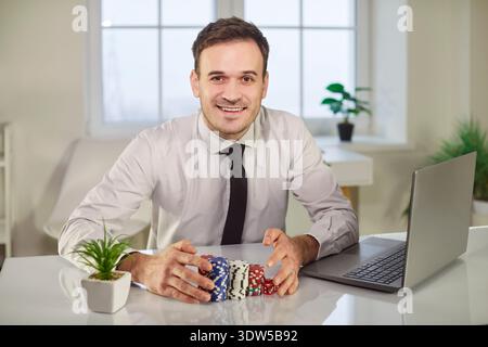 Porträt eines glücklichen lächelnden Mannes, der Poker-Chips hält, der zu Hause sitzt und im Online-Casino gewinnt. Stockfoto