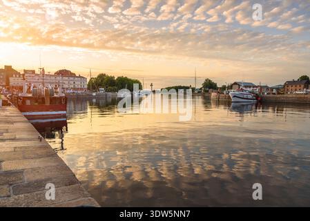 Blick auf einen Fischerhafen unter dramtischem Himmel bei Sonnenuntergang im Sommer. Reflexion im Wasser. Honfleur, Frankreich. Stockfoto