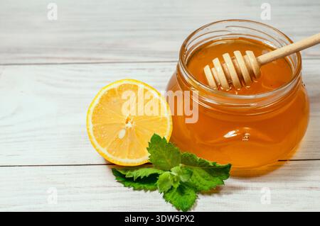 Frischer Honig in einem transparenten Glas auf hölzernem Hintergrund und Zitrone mit Minze Stockfoto