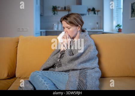 Unwohlsein Frau niest in Gewebe, wischt Nase leidet kalte Symptome sitzt in warme Decke gewickelt. Stockfoto