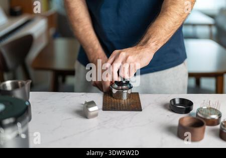 Eine Nahaufnahme zeigt einen erwachsenen Mann, der während der Zubereitung des Espresso Kaffeesatz mit einem Manipulator in einen Portafilter drückt. Das Bild hebt die Präzision hervor, t Stockfoto