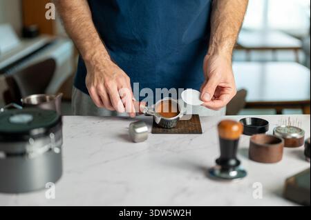 Ein erfahrener Barista, der Papierfilter auf perfekt gemahlenem frisch gemahlenem Kaffee in den Portafilter einsetzt und die Kunst der Espresso-Zubereitung in einem gemütlichen h Stockfoto