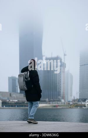 Mann im Wintermantel mit Blick auf eine nebelige Stadtpromenade. Konzept einer städtischen Winteraktivität Stockfoto