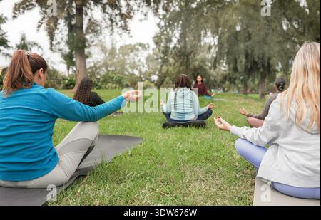Frauen, die im Freien Meditationsübungen im Stadtpark machen - gesunder Lebensstil, Achtsamkeit und Geisteszustand Konzept - Hauptfokus auf die linke weibliche Hand Stockfoto