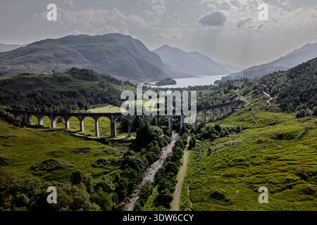 Ein Panorama-Drohnenfoto, das das geschwungene Eisenbahnviadukt, einen gewundenen Fluss und die umliegenden Berge und den See zeigt. Stockfoto