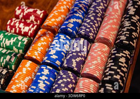 Ordentlich angeordnete Stapel von bunten Pokerchips auf einer Holzoberfläche, die mehrere Stückelungen zeigen, die in Casino-Spielen verwendet werden. Die Chips sind farblich in klaren Reihen angeordnet, wodurch ihre Textur, Muster und Vielfalt hervorgehoben werden. Stockfoto