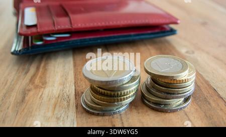 Rote Lederpartikel und Münzen stapeln sich auf dem Holztisch. Geldbörse mit europäischem Geschäftskonzept „Geld für den Handel“. Stockfoto