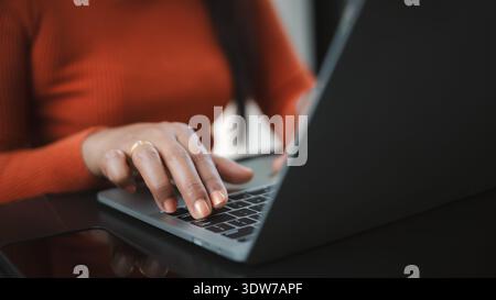 Nahaufnahme der Hände einer Frau mit orangefarbenen Nägeln, die auf einer Laptop-Tastatur tippen. Konzept der Fernarbeit, professioneller Freiberufler, Online-Geschäftskommunikation Stockfoto