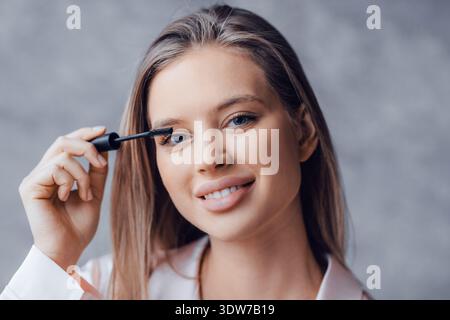 Frau, die Mascara in einer Beauty-Routine zu Hause in natürlichem Licht aufträgt Stockfoto