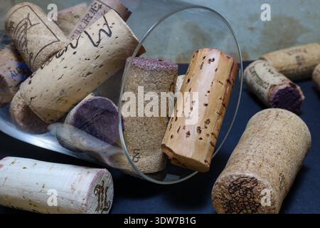 Athen, Griechenland - 15. Februar 2026: Gebrauchte Weinkorken, die um ein umgedrehtes Weinglas auf dunkler Oberfläche verstreut sind. Stockfoto