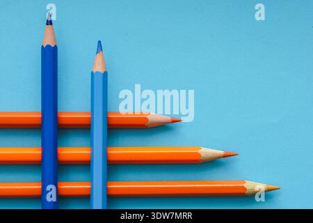 Blaue und orangefarbene Bleistifte, die in dynamischen diagonalen Linien auf einem kräftigen blauen Hintergrund angeordnet sind, veranschaulichen den komplementären Farbkontrast Stockfoto