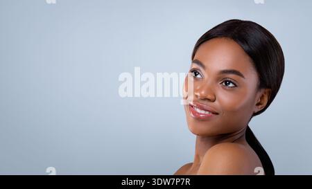 Die schöne Frau lächelt, während sie über ihre Schulter in einem einfachen Studio-Setting schaut Stockfoto