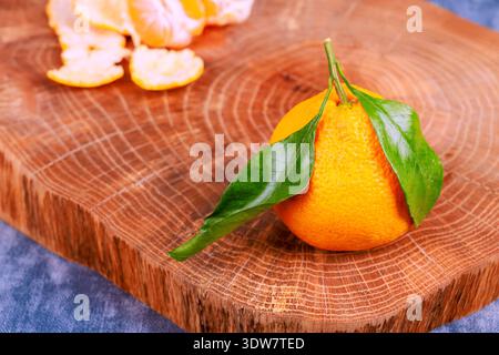 Eine natürliche Bio-Orange steht auf einem hölzernen Schneidebrett mit ihren grünen Blättern, die orange Segmente abblätternd sind in der Nähe platziert. Stockfoto