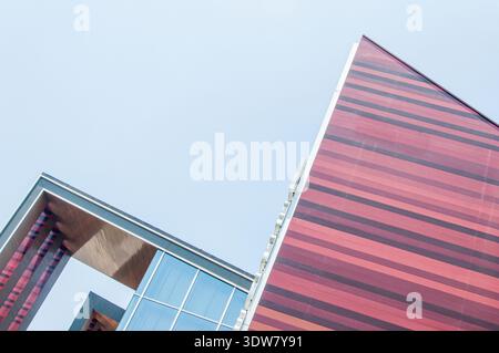Flacher abstrakter Blick auf ein modernes Gebäude mit markanten rot-braunen horizontalen Streifenverkleidungen und Glasfenstern vor blauem Himmel. Stockfoto
