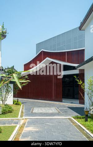 Vertikale architektonische Aufnahme eines modernen Gebäudes mit einer markanten Fassade aus rotbraunen vertikalen Holzlatten, die von einem Steinweg erreicht werden. Stockfoto