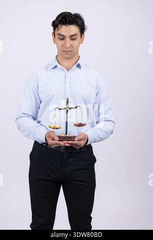 Junger Mann im Hemd, der Waagen der Gerechtigkeit im Atelier hält Stockfoto