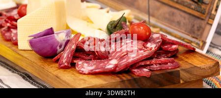 In Scheiben geschnittene Salami- und Käseplatte mit frischem Gemüse, rustikales Gourmet-Vorspeisenkonzept, Banner Stockfoto
