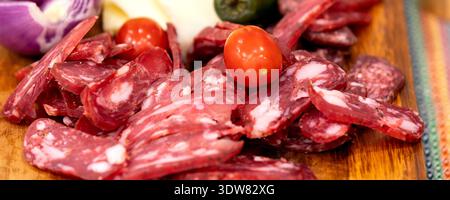 In Scheiben geschnittene Salami- und Käseplatte mit frischem Gemüse, rustikales Gourmet-Vorspeisenkonzept, Banner Stockfoto