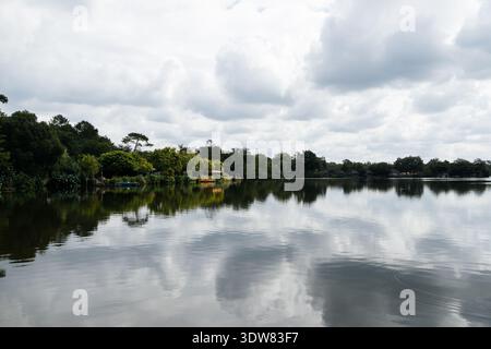 Ruhiges Wasser mit üppigen Bäumen und Himmel mit zwei Booten, die an einem kleinen Dock verankert sind. Soustons See in der Azur Frankreich Stockfoto