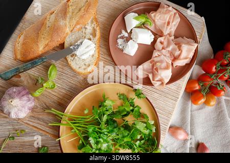 Hochwertige Bauernkost auf hölzernem Schneidebrett. Draufsicht. Flachbild-Foto. Weicher Ziegenkäse auf Brot, Basilikum und Mortadella Sandwich. Italienische Tradition Stockfoto