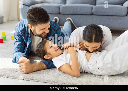 Glückliche Eltern und Kinder, die zu Hause zusammen lachen, spielerisches Kleben auf Teppich Stockfoto