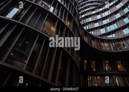 Moderne geschwungene Fassade des Bürogebäudes mit beleuchteten Fenstern in der Abenddämmerung Stockfoto