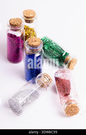 Sechs Glasflaschen stehen auf weißem Hintergrund, jede mit verschiedenen Glitzerfarben gefüllt. Die Flaschen haben Korkstopfen und sind lässig angeordnet Stockfoto