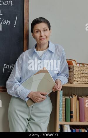 Vertikal einer kaukasischen Frau mittleren Alters, die lächelt, während sie Notebooks hält Stockfoto
