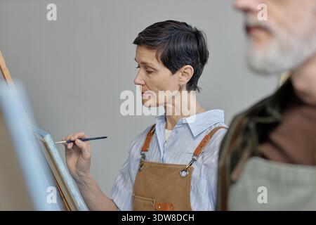 Kaukasische Frau mittleren Alters, die sich beim Erstellen von Kunstwerken im Unterricht konzentriert Stockfoto