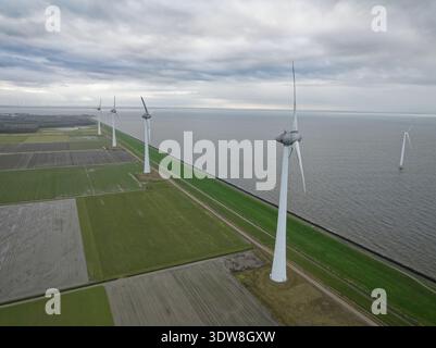 Windturbinen stehen an einem Schutzdeich neben landwirtschaftlichen Feldern und dem Meer Stockfoto