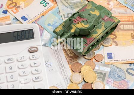 Spielzeugtank auf Geld und Münzen in der Nähe des Taschenrechners und des Bargeldes. Stockfoto