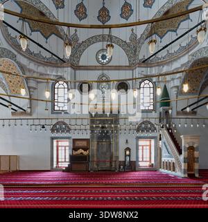 Das Innere des Selimiye Camii, Konya, Türkei, verfügt über kunstvoll verzierte Mihrab, Minibar, reich gemusterte Decken, roten Gebetsteppich und elegante Hängelampen, die islamische Architektur zeigen Stockfoto