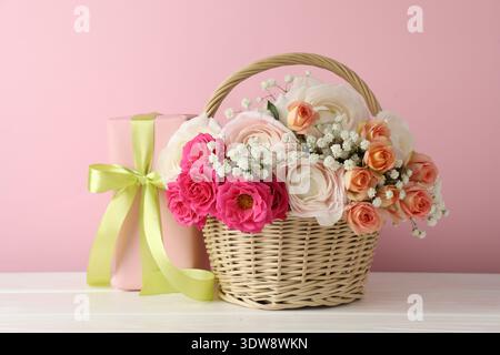 Schöne Blumen im Korb und Geschenk auf weißem Holztisch Stockfoto