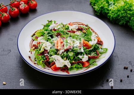 Frischer grüner Salat mit Tomaten, getrockneten Tomaten und cremigem Dressing auf Teller Stockfoto