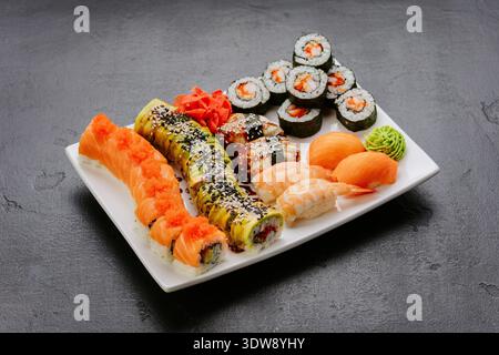 Verschiedene Sushi-Brötchen, Nigiri und Sashimi, serviert auf weißem Teller auf dunklem Hintergrund Stockfoto
