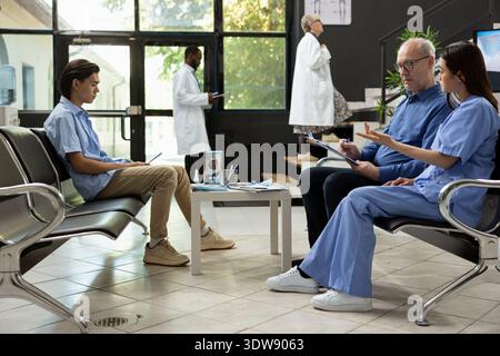 Die Krankenschwester hilft älteren Patienten mit Papierkram und erläutert wichtige Informationen. Medizinisches Fachpersonal kümmert sich um Patienten und veranschaulicht die aktive Klinik oder den Warteraum des Krankenhauses. Stockfoto