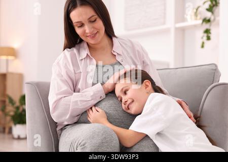 Schwangere Frau und ihre Tochter sitzen zu Hause auf einem Sessel Stockfoto