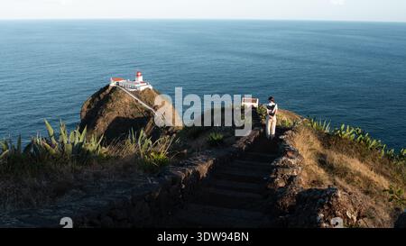 Santa Maria Island, Azoren, Portugal - 16. September 2024: Person, die auf einem Steinweg auf einer Klippe zum Leuchtturm von Gonzalo Velho geht, mit einer dramatischen Wanne Stockfoto