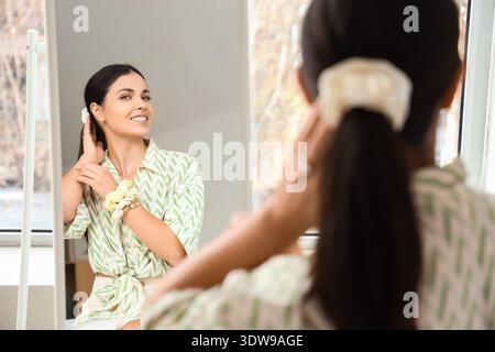 Wunderschöne Frau mit Pferdeschwanz und Scrunchies in der Nähe des Spiegels im Schlafzimmer Stockfoto