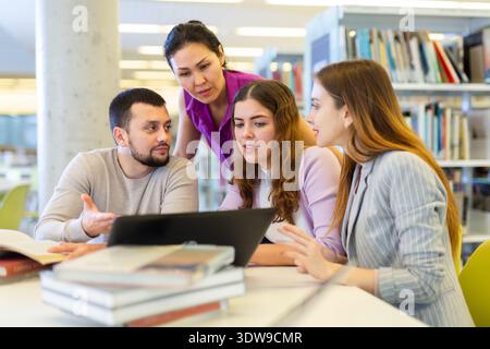 Fröhliche Studenten studieren in der Bibliothek mit Büchern und Laptop Stockfoto